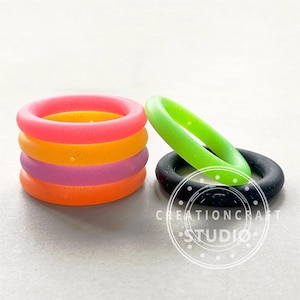 May include: A set of five silicone rings in various colors, including pink, orange, purple, and green. The rings are stacked on top of each other, with a black silicone ring lying next to them.