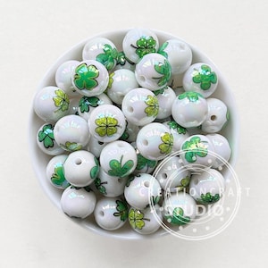 May include: A bowl of white and iridescent beads with green four-leaf clover designs. The beads are perfect for crafting jewelry or other projects.