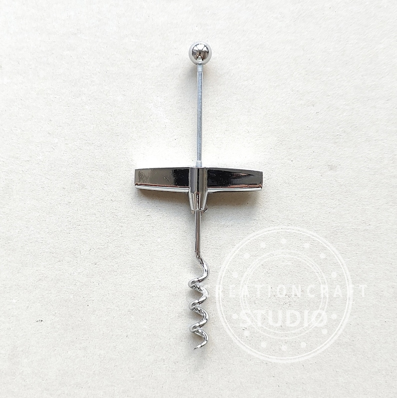 May include: A silver corkscrew with a T-shaped handle and a spiral corkscrew. The corkscrew has a ball on the top of the handle.