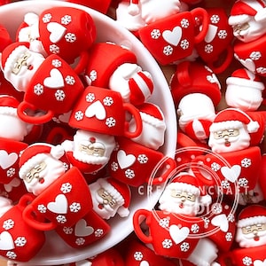 Pode incluir: Uma coleção de mini canecas e figuras do Papai Noel com tema natalino. As canecas vermelhas apresentam corações brancos e flocos de neve. As figuras do Papai Noel usam chapéus vermelhos e têm barbas brancas. Os itens estão espalhados em uma tigela branca.