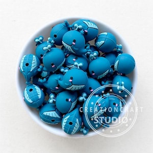 Könnte beinhalten: Eine Schüssel gefüllt mit tealblauen Silikon-Walperlen. Die Perlen haben einen weißen Umriss und einen kleinen rosa Mund.