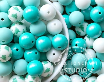 May include: A collection of round beads in various shades of blue and white. Some beads are solid colors, while others feature a repeating Christmas tree pattern. The beads are arranged in a white bowl, with the "CreationCraft Studio" logo visible.
