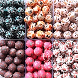 May include: A selection of patterned beads in a variety of colours. The round beads display designs including floral, geometric, and fruit patterns. The colour scheme includes black, teal, pink, red, orange, and white.