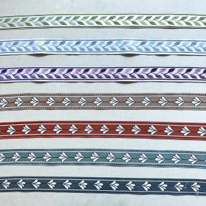 Könnte beinhalten: Sechs verschiedene Bänder mit einem weißen Blumenmuster auf beigefarbenem Hintergrund. Die Bänder sind in den Farben Grün, Blau, Lila, Braun, Rot und Grau.