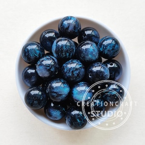 May include: A bowl of dark blue and black round beads with a glittery finish. The beads have a swirling pattern and are approximately 2 cm in diameter.
