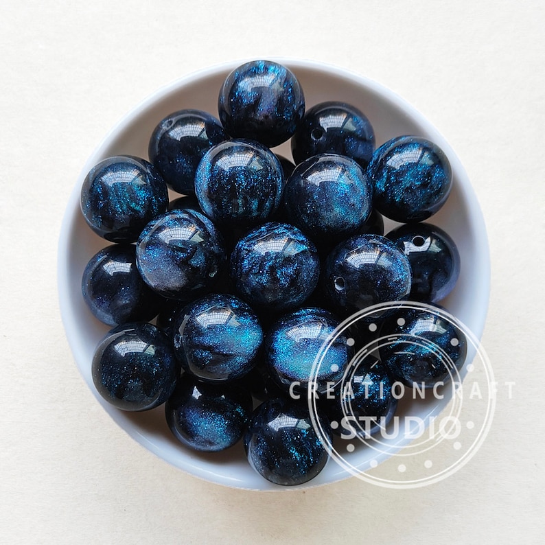 May include: A bowl of dark blue and black round beads with a glittery finish. The beads have a swirling pattern and are approximately 2 cm in diameter.