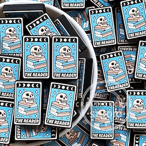 Może przedstawiać: Kolekcja niebieskich i białych amuletów do kart tarota z motywem czaszki i skrzyżowanych kości z tekstem "The Reader".