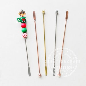 Può includere: Una collezione di agitatori per cocktail decorativi. Un agitatore presenta un design a renna e tazza, mentre altri hanno finiture metalliche in rame, oro e argento. Gli agitatori sono progettati per mescolare le bevande e aggiungere un tocco festivo.