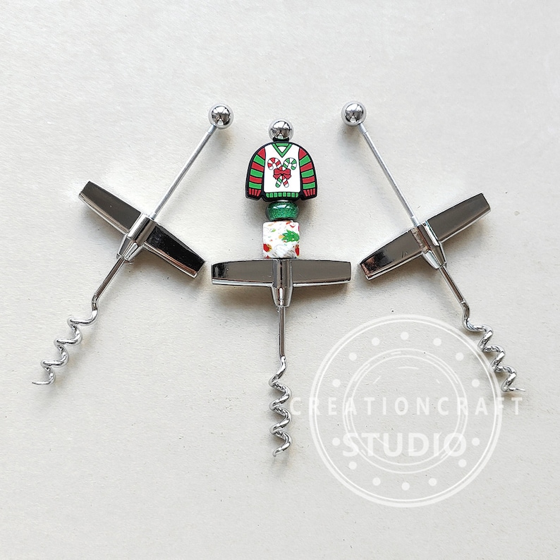 May include: Three silver wine bottle openers with a Christmas sweater design. The sweater is red, green, and white with candy canes and holly.