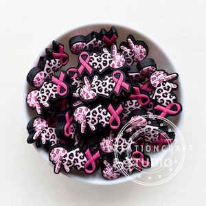 Könnte beinhalten: Eine Schüssel gefüllt mit rosa und schwarzen Gummianhängern mit einem rosa Band und einem Peace-Zeichen. Die Anhänger sind mit einem Leopardenmuster verziert.