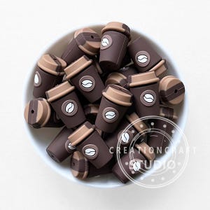 May include: A collection of brown and tan coffee cup-shaped beads with a coffee bean design. The beads are in a white bowl. The text "CREATIONCRAFT STUDIO" is visible on the right side of the image.