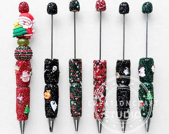 May include: A collection of decorative pens with various holiday-themed designs. The pens feature red, black, and green beaded barrels, with Santa Claus, snowman, and Halloween-themed accents. The pens have silver tips and are arranged on a white surface.