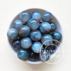 May include: A bowl filled with blue and black iridescent glass beads. The beads have a shimmery, glittery finish.