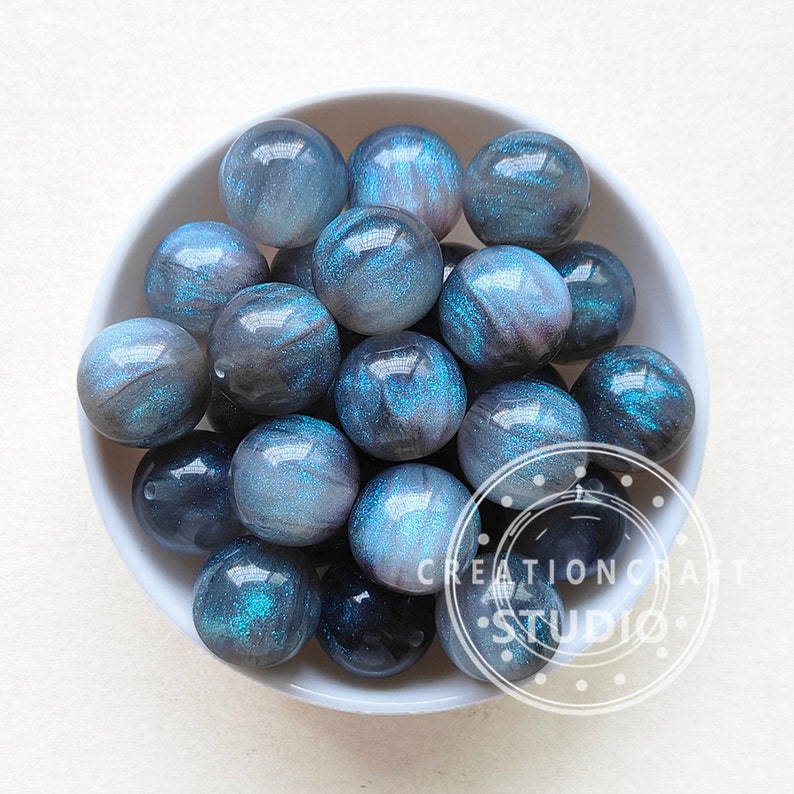 May include: A bowl filled with blue and black iridescent glass beads. The beads have a shimmery, glittery finish.