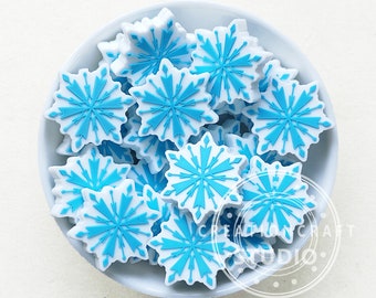 Puede incluir: Un tazón blanco lleno de abalorios en forma de copo de nieve azul y blanco. Los copos de nieve tienen un fondo blanco con un diseño de copo de nieve azul.