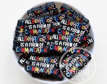 May include: A close-up of a pile of black silicone charms with the text "All behavior is a form of communication" in colorful letters.