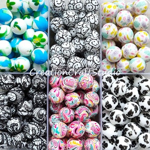 May include: Assortment of colourful silicone beads in various patterns, including smiley faces, swirls, paw prints, and floral designs. The beads are arranged in six clear plastic containers.