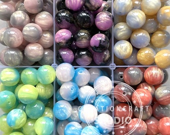 May include: Assortment of colourful iridescent beads in six different colours. The beads are arranged in six separate compartments. The colours are pink, purple, gold, blue, green, and red.