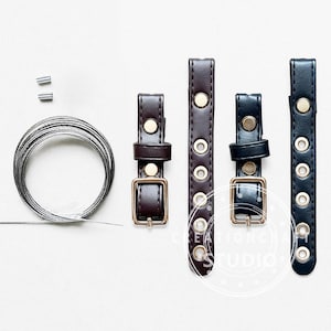 May include: A set of two dark brown and two black faux leather straps with gold-toned metal buckles and eyelets, accompanied by a coiled silver-toned wire and two small metal crimp beads, arranged on a plain surface for craft assembly.