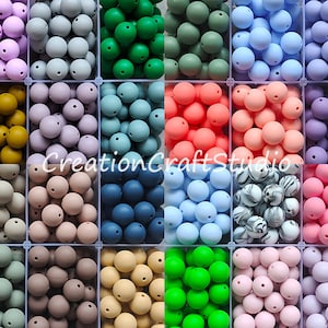 Pode incluir: Conjunto de contas de silicone em várias cores, incluindo azul claro, rosa claro, cinza, verde, marrom e branco. As contas estão dispostas em um padrão de grade em um recipiente de plástico transparente. CreationCraftStudio.
