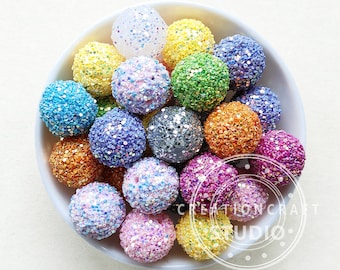 May include: A bowl filled with colorful glitter beads. The beads are various shades of blue, green, purple, pink, orange, yellow, and white. The beads are all round and have a sparkly finish.