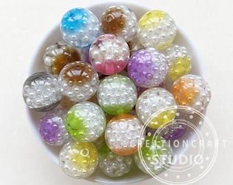 May include: A bowl filled with colorful, translucent, round beads. Each bead is covered in small white pearls. The beads are in various colors, including purple, green, yellow, orange, pink, and blue.