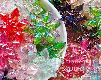 May include: A bowl filled with iridescent snowflake ornaments in various colors, including red, green, pink, and purple. The snowflakes are made of a clear material with a shimmering finish.