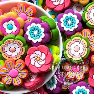 Op de afbeelding: Een kom vol kleurrijke, fantasievolle bloemvormige bedels. De bedels zijn gemaakt van siliconen en hebben verschillende kleuren, patronen en ontwerpen. De bedels zijn perfect om elke creatie een vleugje plezier en persoonlijkheid te geven.