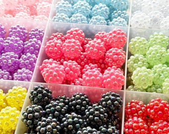 May include: A segmented container filled with colourful, clustered beads. The beads are in various shades, including pink, blue, white, purple, green, yellow, black, and red. The beads have a textured, bumpy surface, resembling small berries.