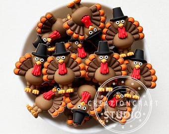 May include: A collection of brown turkey-shaped embellishments with orange and brown tail feathers, red wattles, and black top hats. The turkeys are in a white bowl. The text "CREATIONCRAFT STUDIO" is visible.
