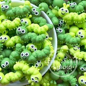 May include: A bowl filled with green and lime green caterpillar-shaped beads with smiling faces. The beads are made of silicone and are perfect for sensory play or crafting.
