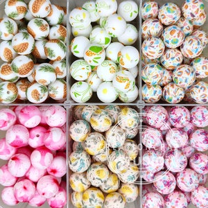 May include: Assortment of decorative beads in various designs. The beads are white with colorful patterns, including pineapples, floral, and abstract designs. The beads are round and have a hole for stringing.