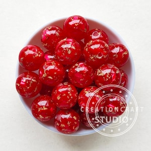May include: A bowl of red and gold beads. The beads are round and have a shiny finish. They are ideal for making jewellery or other crafts.