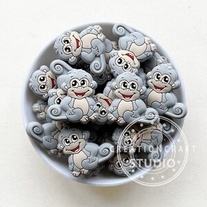 May include: A bowl filled with gray silicone monkey charms. The monkeys have white faces with black eyes and a red smile.