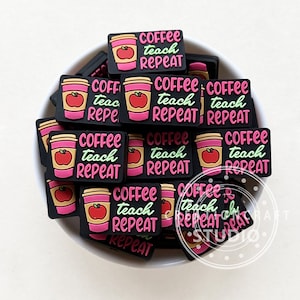 Puede incluir: Un bol lleno de dijes de taza de café negros y rosados con el texto "Coffee teach repeat" en cada dije. Los dijes están decorados con una manzana roja y una taza de café amarilla.