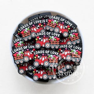 Può includere: Una ciotola piena di trattori giocattolo rossi con ruote nere e un cassone bianco pieno di cuori colorati. I trattori hanno la scritta "Loads of Love".