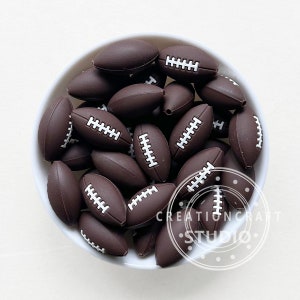 May include: A bowl filled with brown silicone football-shaped beads. The beads have white stitching details.