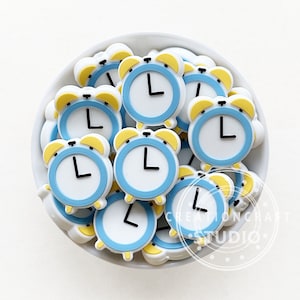 May include: A bowl filled with blue and yellow alarm clock shaped charms. The charms have white faces with black hands and a black outline.
