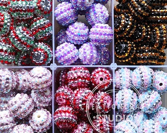 May include: Assortment of colorful, sparkly, round beads in a plastic storage container. The beads are arranged in rows and are various shades of pink, purple, blue, green, and black.