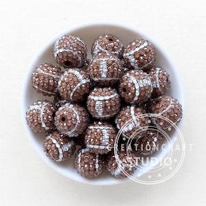 May include: A bowl filled with brown and white football-shaped beads. The beads are covered in rhinestones.