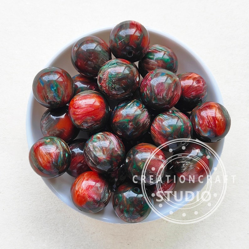 Pode incluir: Uma tigela de contas redondas de resina coloridas com redemoinhos de vermelho, verde e dourado. As contas t&ecirc;m um di&acirc;metro aproximado de 2,5 cm.