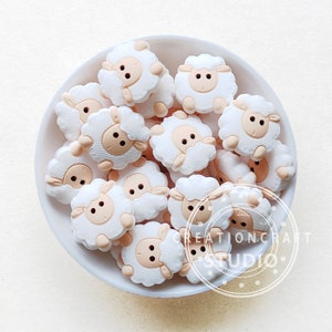 May include: A bowl filled with white and beige sheep-shaped buttons. The buttons have a textured surface and black eyes.