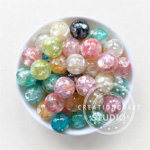 May include: A bowl filled with colorful iridescent round beads. The beads are made of plastic and have a variety of colors, including pink, blue, green, and yellow. The beads are perfect for crafting and jewelry making.