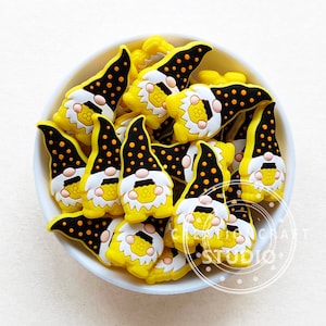 May include: A bowl filled with yellow and black gnome-shaped charms. The gnomes have black polka dots and white faces.