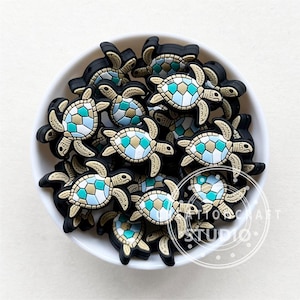 May include: A bowl filled with small, colourful, silicone turtle charms. The turtles have a mosaic pattern of blue, green, and gold.