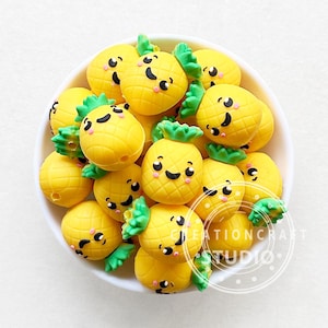 May include: A bowl filled with yellow pineapple-shaped silicone beads with green tops and happy faces. The beads are perfect for sensory play or as a necklace.