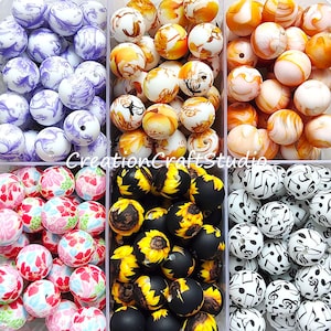 May include: Six containers of colourful, patterned beads. The beads are arranged in rows and are all the same size. The beads are made of a smooth, glossy material. The containers are clear plastic and have a white background. The beads are in the following patterns: floral, sunflower, musical notes, paisley, autumn leaves, and swirls.