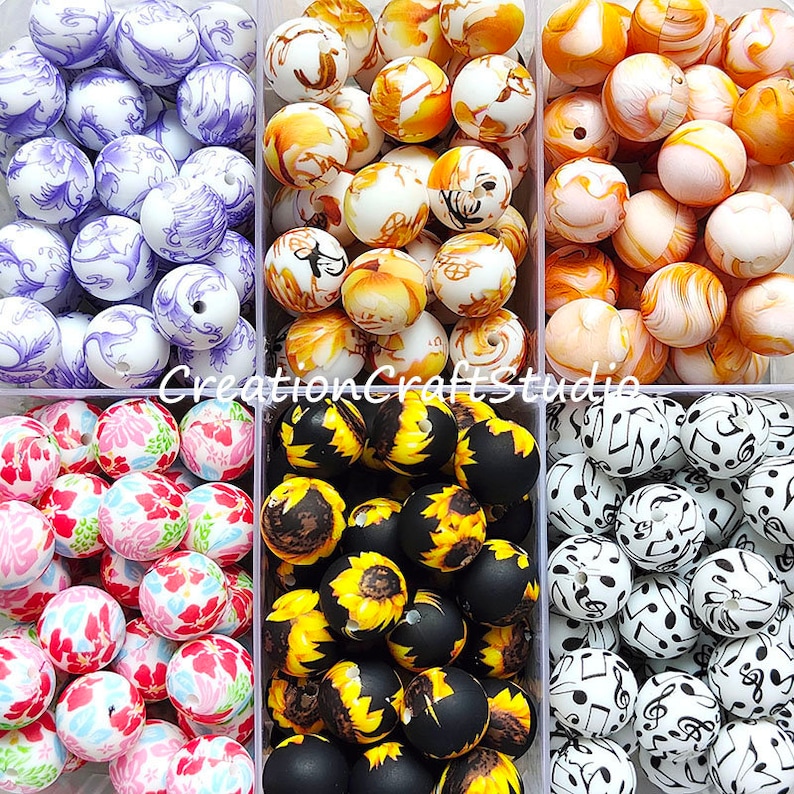May include: Six containers of colourful, patterned beads. The beads are arranged in rows and are all the same size. The beads are made of a smooth, glossy material. The containers are clear plastic and have a white background. The beads are in the following patterns: floral, sunflower, musical notes, paisley, autumn leaves, and swirls.