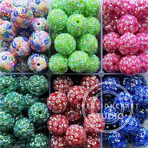 May include: Assortment of colorful, sparkly, round beads with a starburst design. The beads are arranged in rows in a clear plastic container.