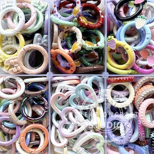 以下が含まれることがあります： 円形、ハート、イチゴなど、さまざまな形をしたカラフルなプラスチック製のキーホルダーの詰め合わせ。キーホルダーは6つの別々のコンパートメントに整理されています。